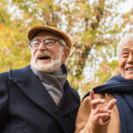 Low angle view of grey haired asian man pointing with finger near multiethnic friends in autumn park, banner,stock image